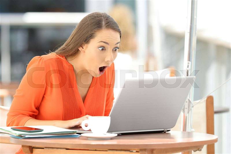 Single astonished student finding amazing content on line in a laptop sitting in a restaurant, stock photo