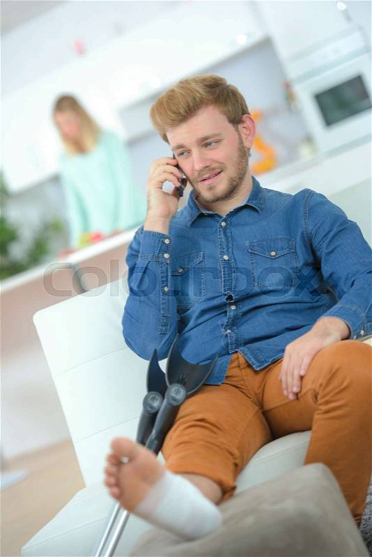 Young man with plastered leg talking on mobile phone, stock photo