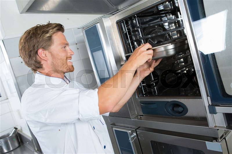 Smiling handsome male cook holding dish in the restaurant kitchen, stock photo