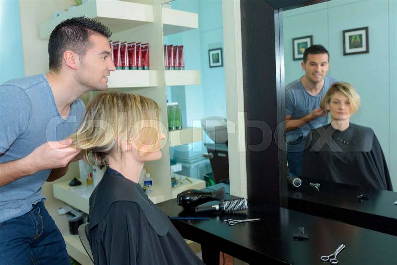 Male hairstylist is making a haircut for a happy woman, stock photo