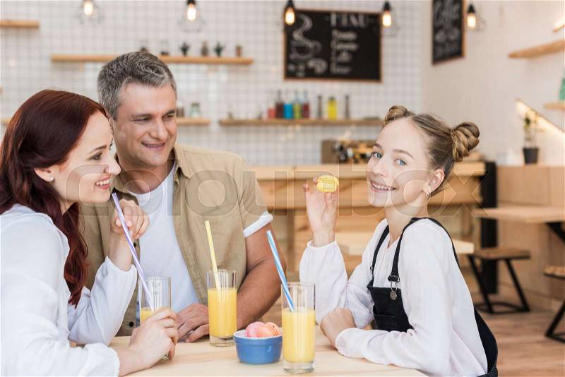 Beautiful family with macaroons and juice in cafe, stock photo