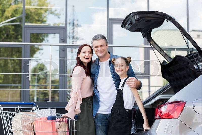 Beautiful happy family with shopping cart next to car, stock photo