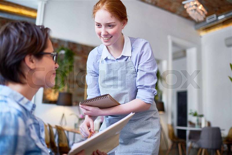 Smiling ginger-head waitress serving one of clients of cafe, stock photo
