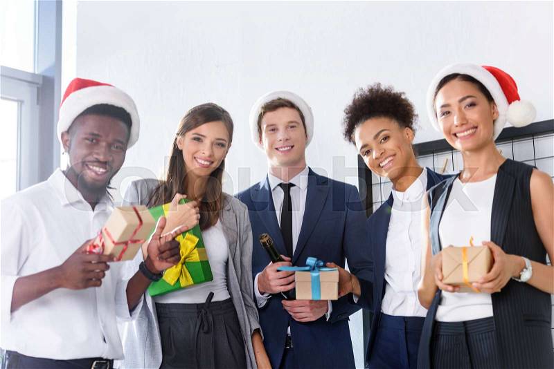 Happy young multiethnic business people holding gifts and smiling at camera in office , stock photo