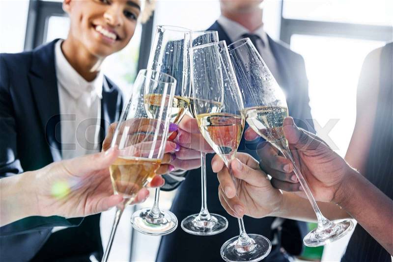 Cropped shot of young business colleagues drinking champagne in office, stock photo