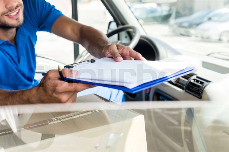 Close-up shot of delivery man with clipboard sitting on van, stock photo