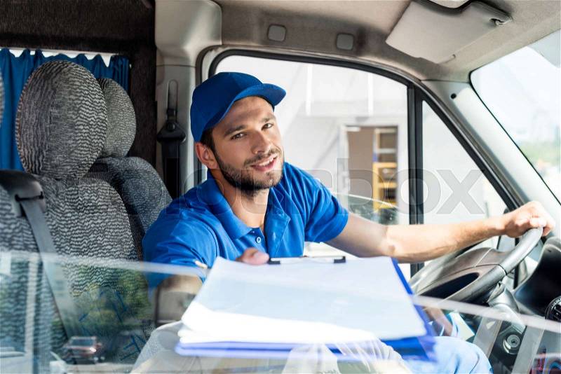 Delivery man with clipboard sitting on van, stock photo