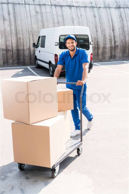 Happy delivery man with cardboard boxes on cart, stock photo