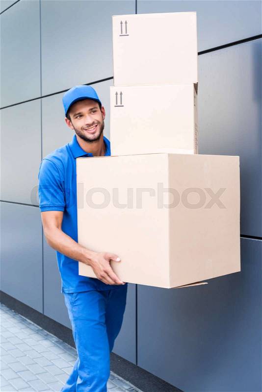 Happy delivery man with stack of cardboard boxes, stock photo