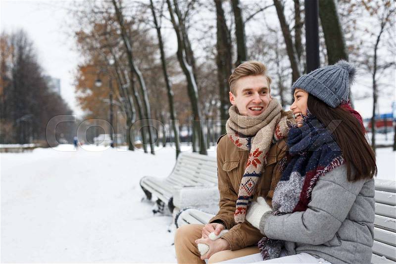Young couple sitting on bench in park and having talk, stock photo