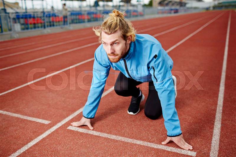 Ambitious athlete standing by starting line on stadium racetrack, stock photo