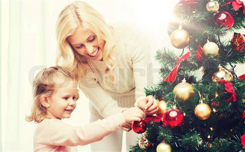 Family, x-mas, winter holidays and people concept - happy mother and little daughter decorating christmas tree at home, stock photo