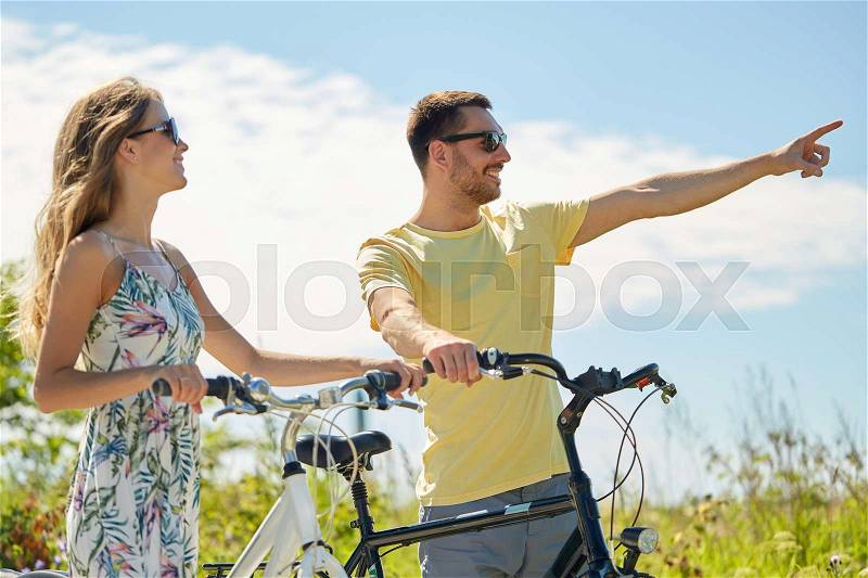 People, direction and lifestyle concept - happy young couple with bicycles at country in summer, stock photo