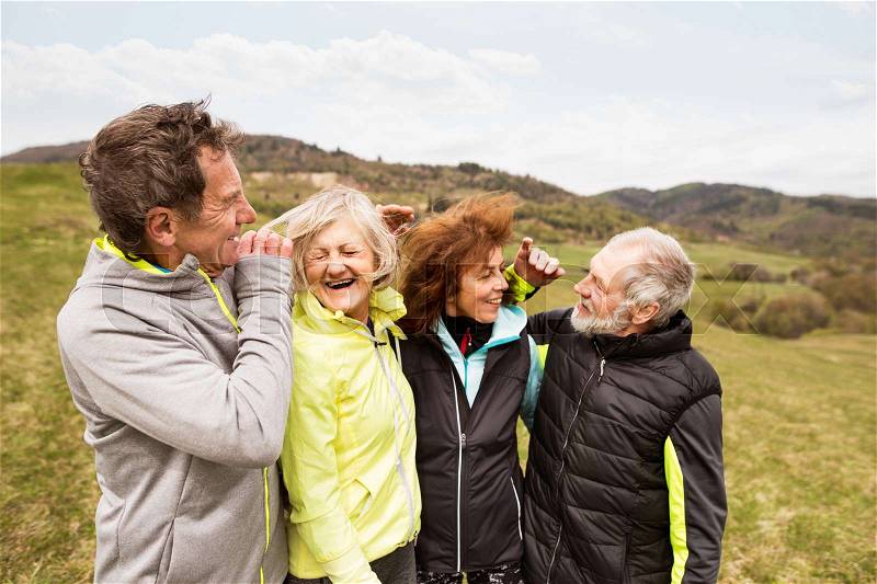 Group of active senior runners outdoors, resting and hugging in windy cold weather, stock photo