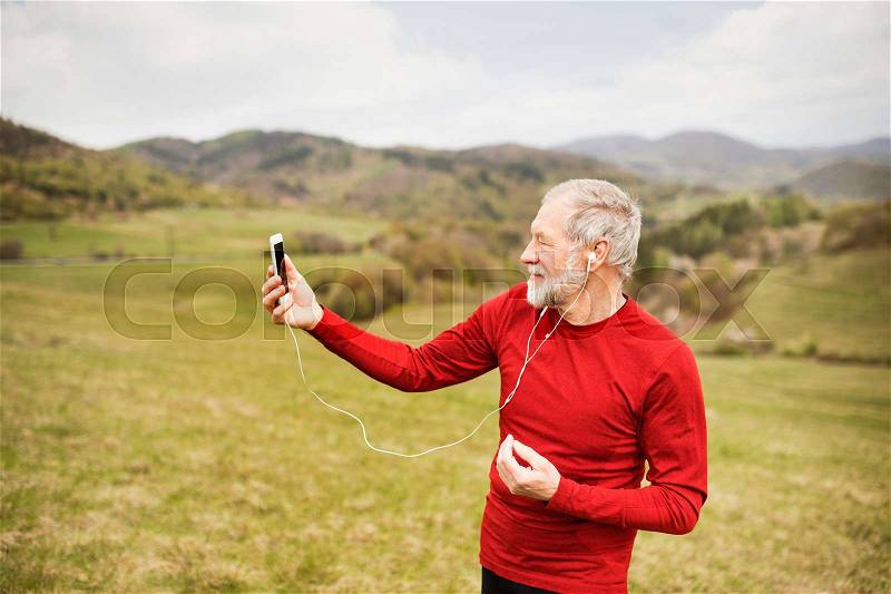 Active senior runner outside on the green hills taking selfie with smart phone, stock photo
