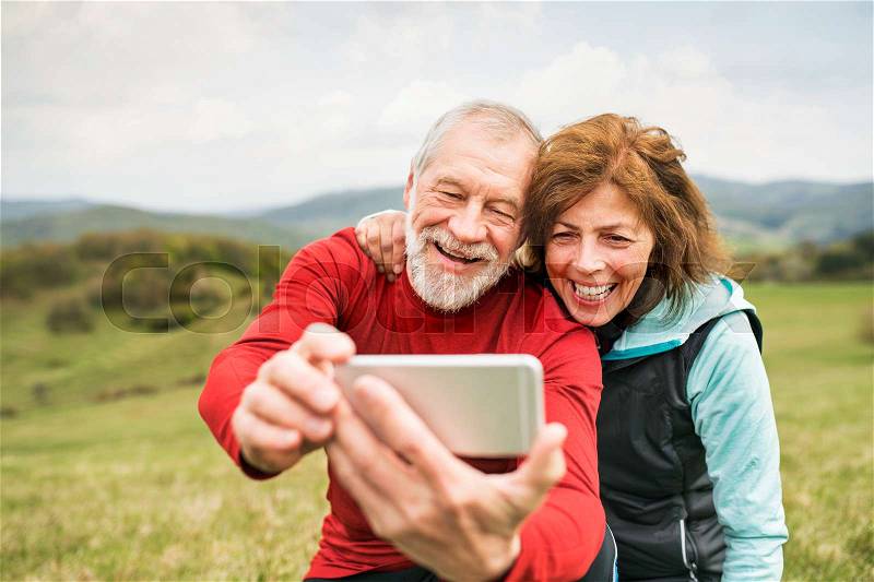 Active senior runners outside on the green hills taking photo with smart phone. Calvary in Banska Stiavnica, Slovakia, stock photo