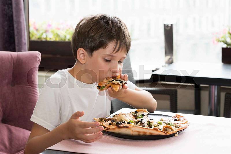 The boy is eating pizza in an Italian restaurant, stock photo