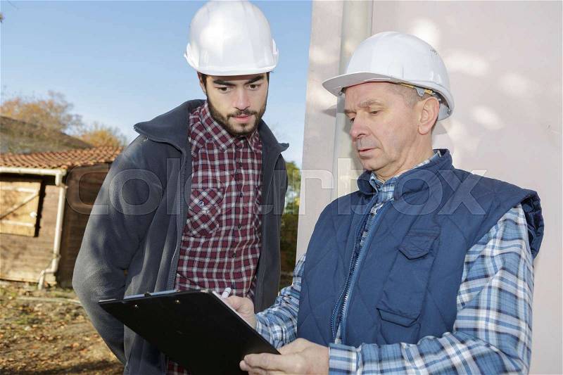 Mature contractor checking his clipboard while talking to co-worker, stock photo