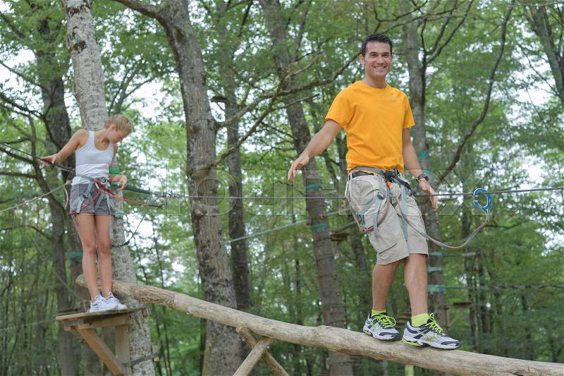 Couple walking on suspended trunk at the adventure park, stock photo