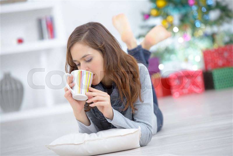 Woman with cup of tea laying on floor at home, stock photo