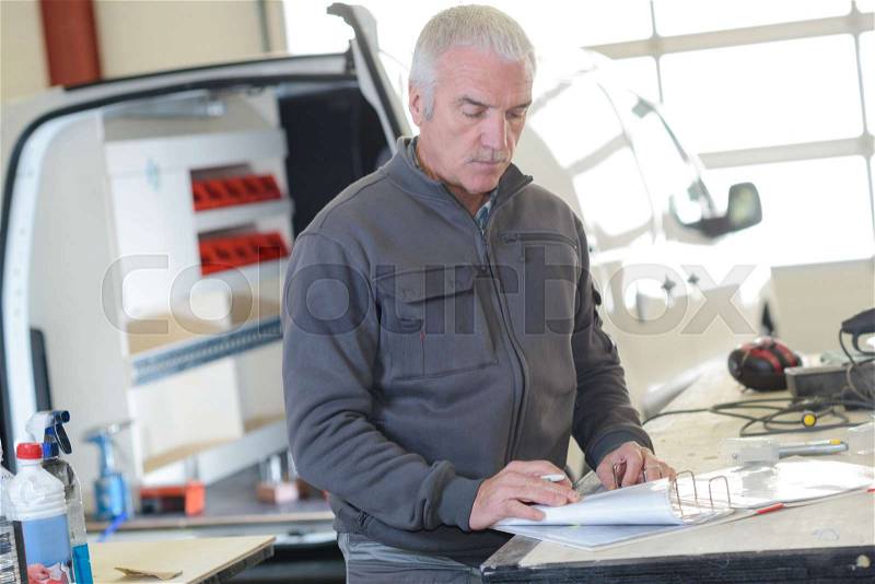 Senior delivery man with a paper box indoors, stock photo
