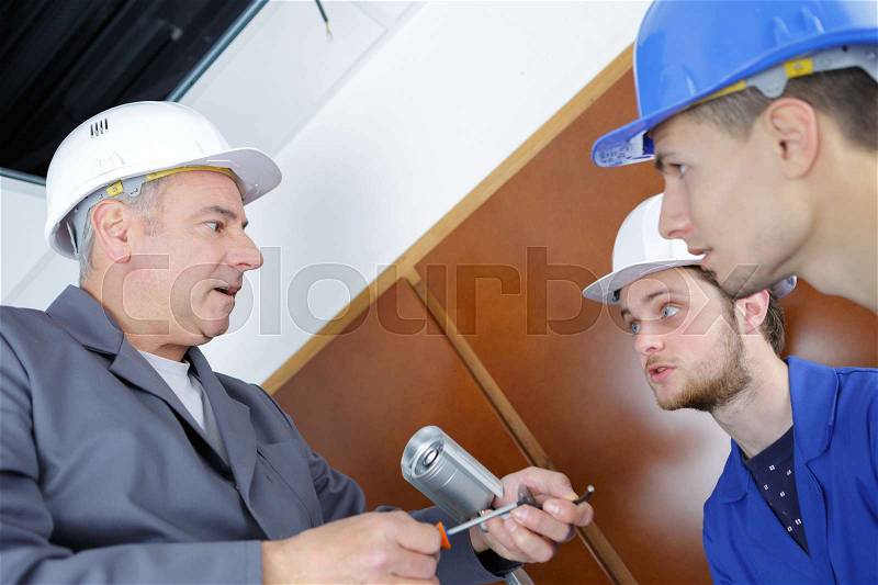 Young technicians learning to installing camera in building corner, stock photo