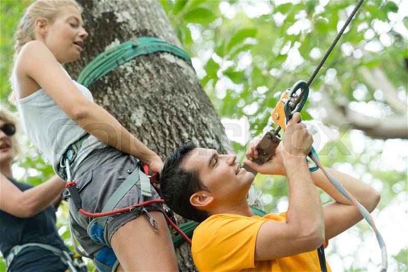 Boyfriend preparing rope for girlfriend in an adventure park, stock photo