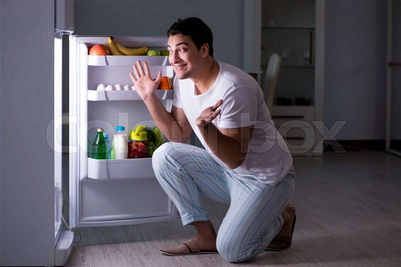 Man at the fridge eating at night, stock photo