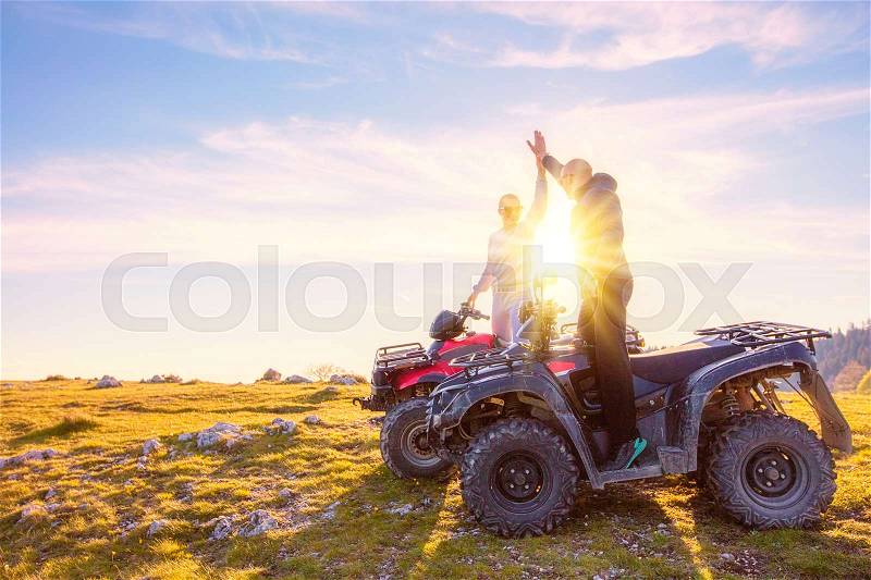 Rear view of young pair near atv. Man is showing something in distance to her girlfriend. Blurred autumn landscape mighty mountains and forests on background, stock photo