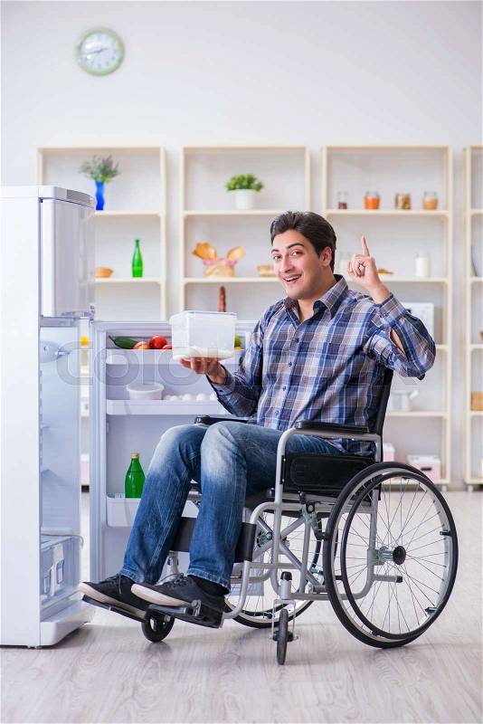 Young disabled injured man opening the fridge door , stock photo