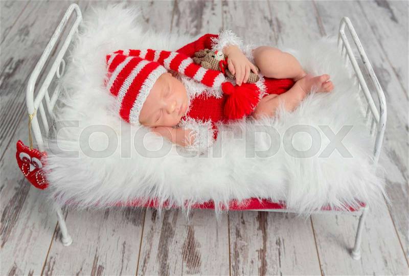 Cute sleeping newborn baby in red hat on little bed with fluffy blanket, stock photo