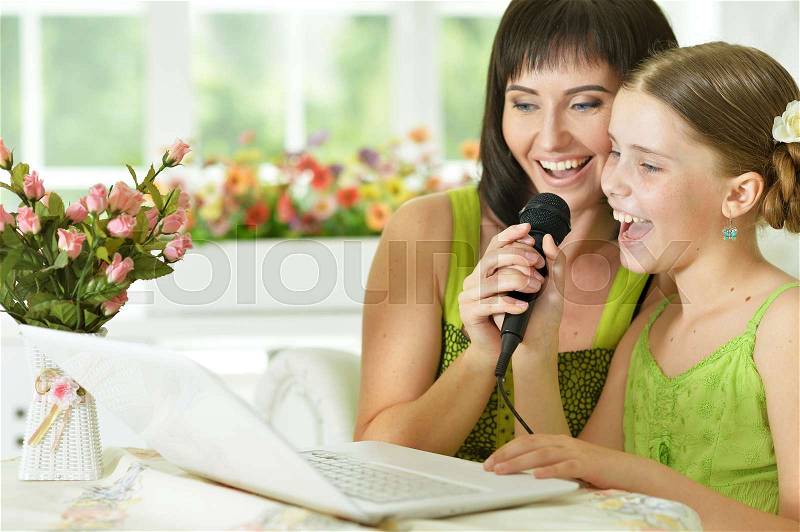 Mother and daughter sitting at table and singing karaoke together, stock photo