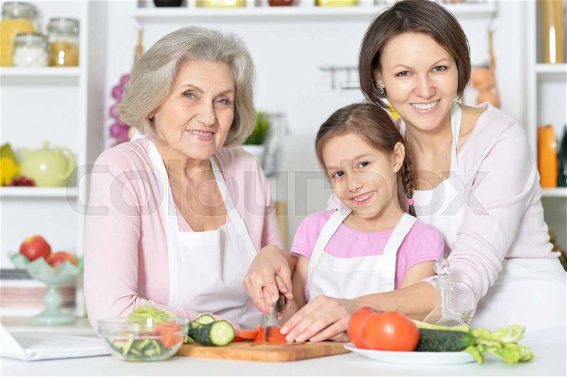 Smiling mother, daughter and grandmother cooking together at kitchen, stock photo
