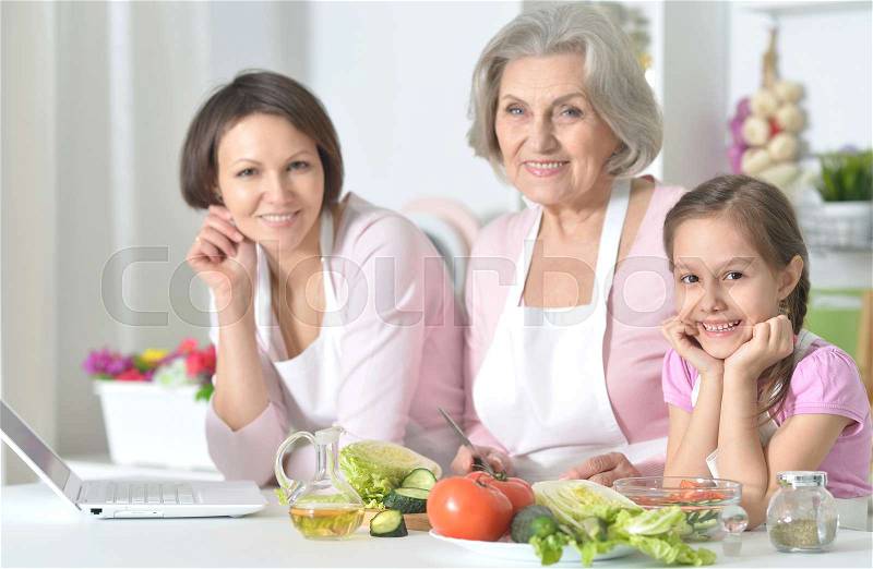 Smiling mother, daughter and grandmother cooking together at kitchen, stock photo