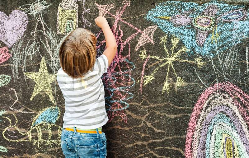 Adorable little boy drawing with a chalk outdoors. Outside activities for children. Back view, stock photo