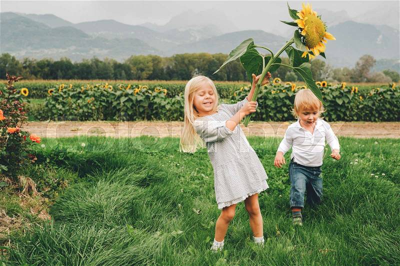 Group of 2 funny kids playing together in flower fields, vacation in countryside with children. Happy active childhood. Family enjoying nature in summer, stock photo