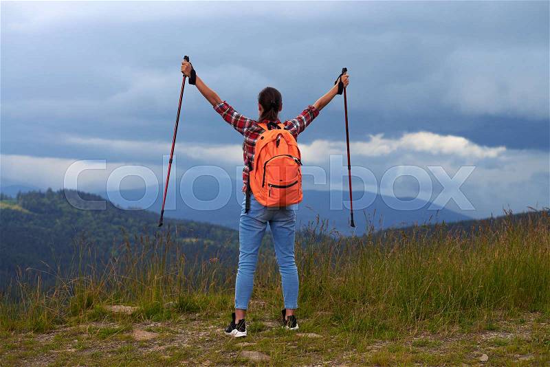 Rear view of young female with hiking poles outstretched hands. Female hiker with backpack , stock photo