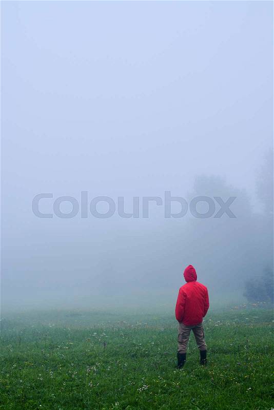 Rear view of man in waterproof jacket standing in the morning in fog , stock photo