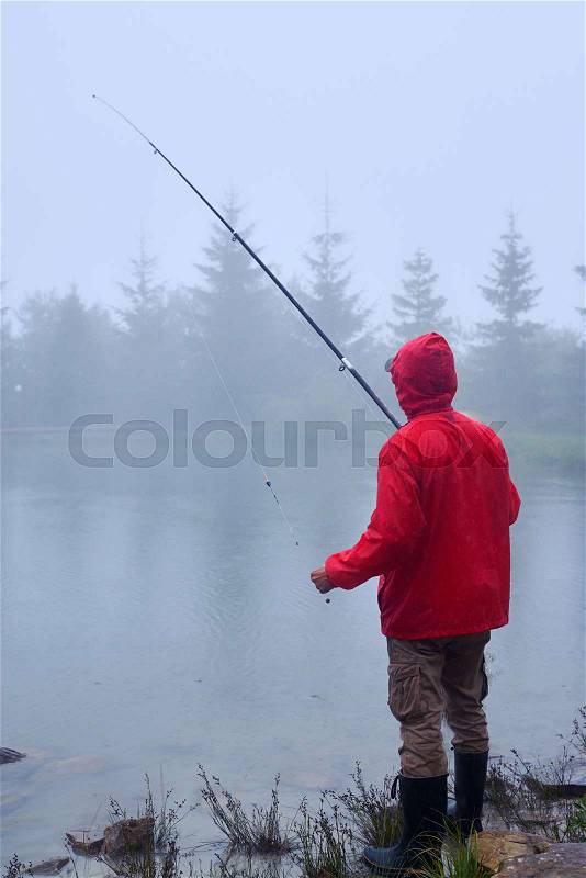 Side view of man in waterproof jacket fishing on rainy weather, stock photo