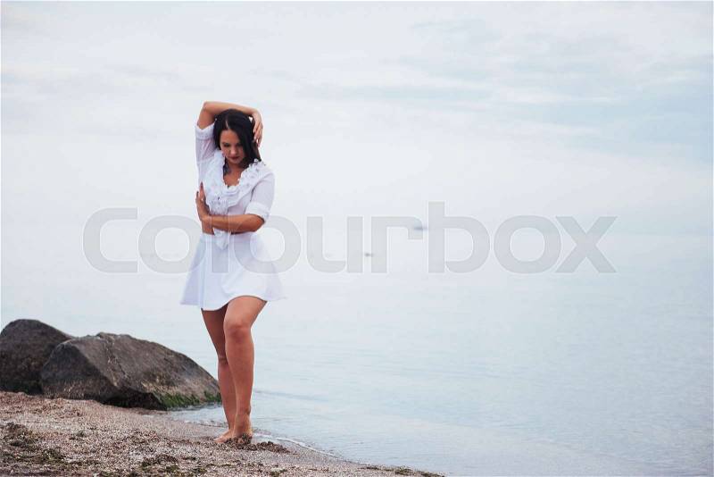 Woman in a white shirt and skirt dancing barefoot on the sand beach hand above the azure sea breeze shakes her long hair, stock photo