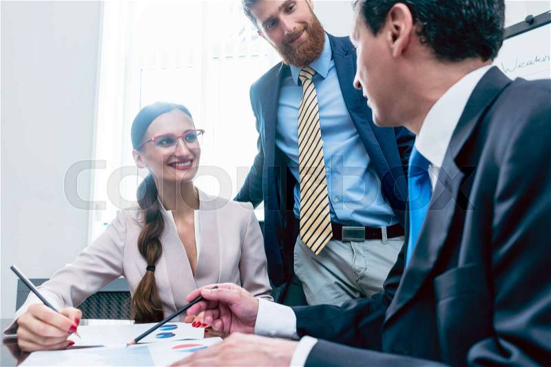 Business analyst smiling while interpreting financial reports showing profit and development during meeting with his female colleagues in the office, stock photo