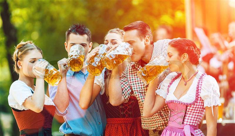 In Beer garden in Bavaria, Germany - friends in Tracht, Dirndl and Lederhosen and Dirndl standing in front of band, stock photo