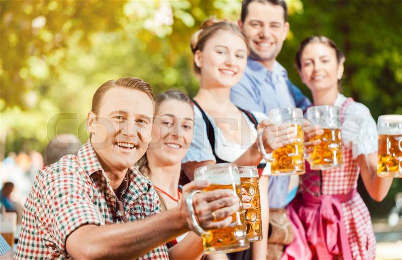 In Beer garden - friends in Tracht, Dirndl and Lederhosen drinking a fresh beer in Bavaria, Germany, stock photo
