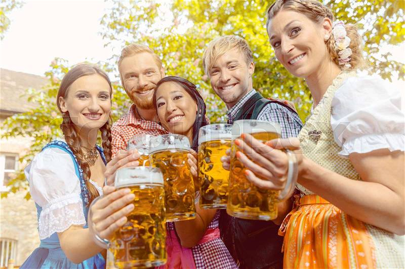 Friends, two men, three women, standing in beer garden with beer glasses, stock photo