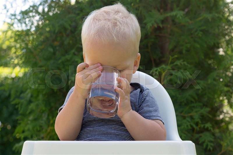 Portrait of one years old blonde caucasian child drinking water in crystal glass outdoors, stock photo