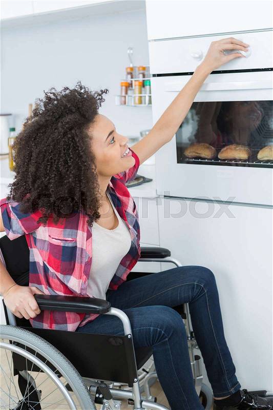 Disabled young woman in wheelchair opens the oven, stock photo