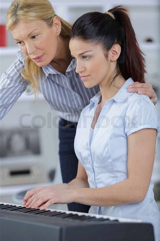 Woman and daughter playing piano and smiling, stock photo
