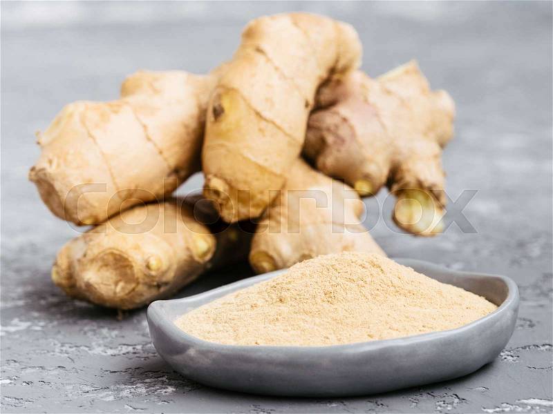 Close up view of ginger poder and ginger root on gray concrete background, stock photo