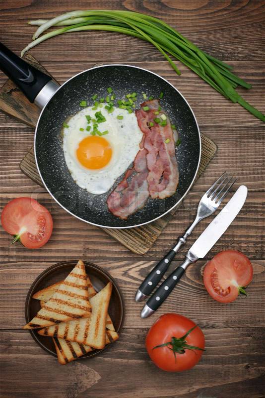 Bacon with sunny side up egg on pan served with tomato and toasts top view, stock photo