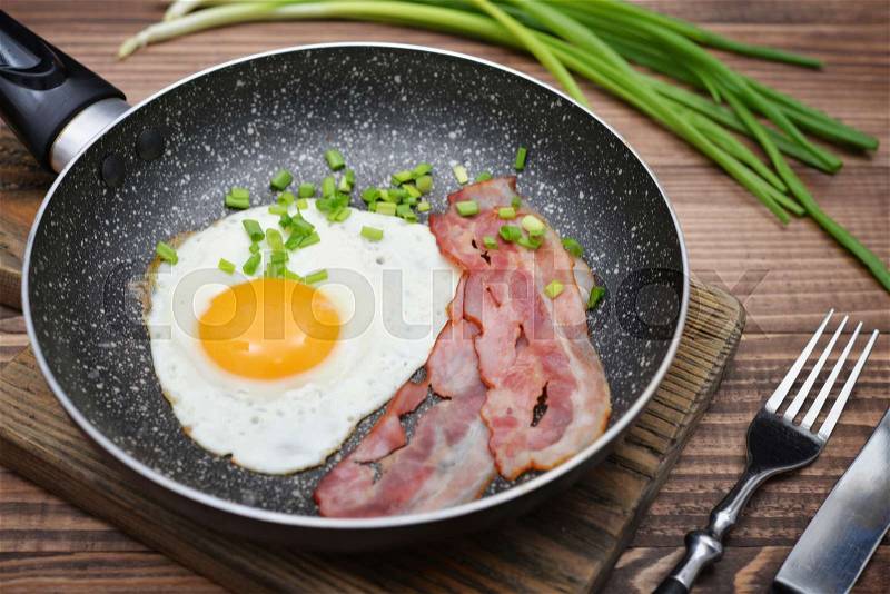 Bacon with sunny side up egg served with bacon and cherry tomato on pan closeup, stock photo